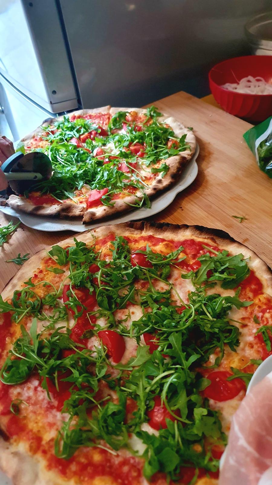 Fresh pizzas topped with arugula and cherry tomatoes during a pizza lesson in Tuscany